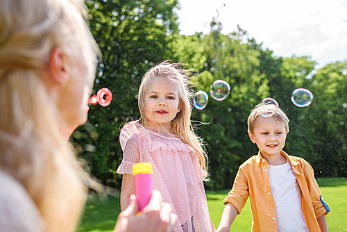 selective focus on mother blowing soap bubbles while spending time with kids in park