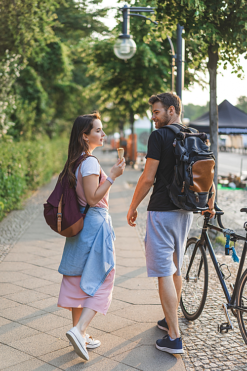 young man with bicycle walking near girlfriend while she eating ice cream at city street