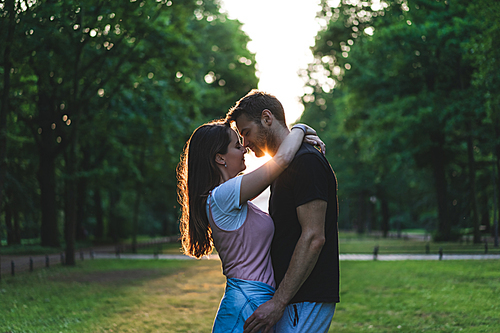 side view of woman embracing boyfriend and kissing him on meadow in park