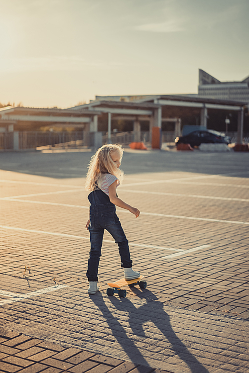 rear view of adorable kid standing with skateboard at parking lot