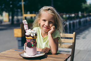 portrait of happy adorable child sitting at table with delicious dessert in cafe