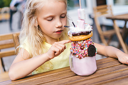 selective focus of adorable little kid pointing by finger on dessert table in cafe