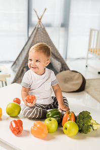 cute smiling toddler sitting on table surrounded by fruit and vegetables