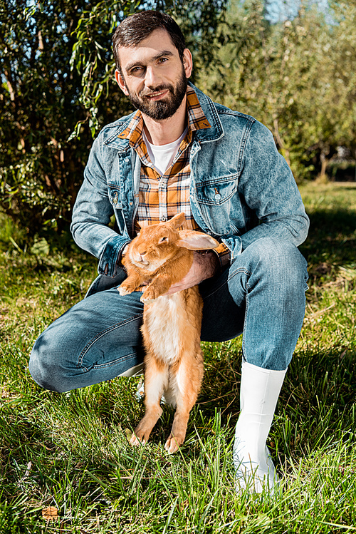 happy male farmer holding brown rabbit  and  outdoors