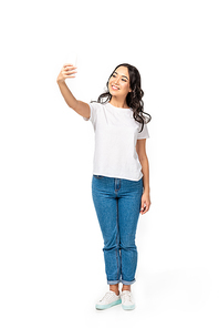 Smiling asian girl in white t-shirt and blue jeans taking selfie isolated on white
