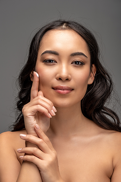 beautiful asian girl applying cosmetic cream on face and  isolated on grey