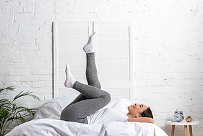 asian woman in white t-shirt and grey leggings doing exercises in bed