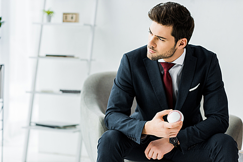 businessman in formal wear sitting on armchair and holding golf ball in office