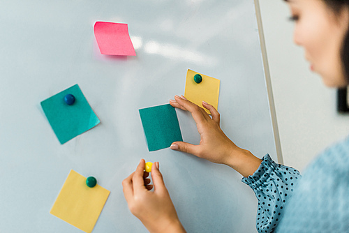 cropped view of woman putting colorful sticky notes on white board in office