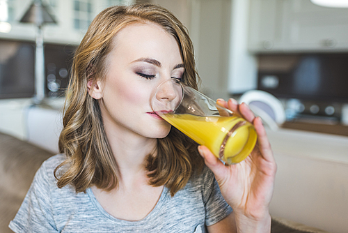 Attractive young woman drinking orange juice on sofa