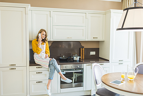 Attractive young woman talking on phone in kitchen