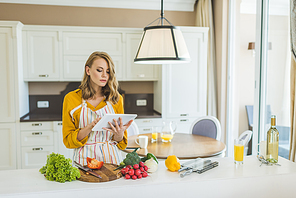 Woman Using Digital Tablet In Kitchen For Recipe