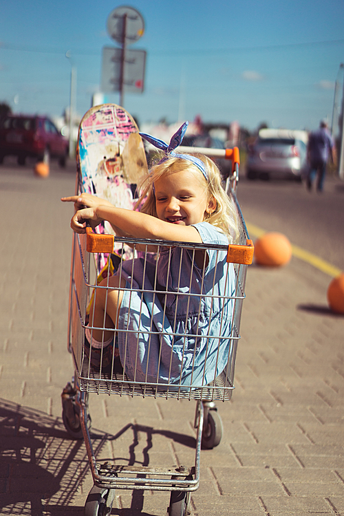 little adorable smiling kid sitting in shopping cart with skateboard