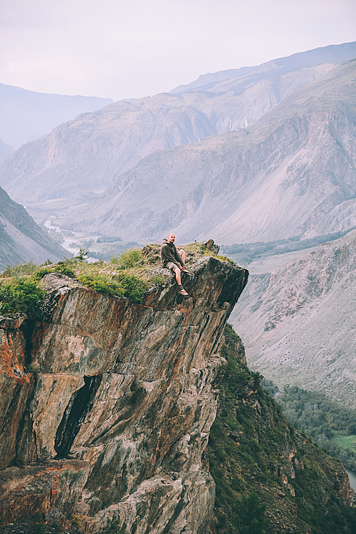 man sitting on cliff and looking at majestic mountains in Altai, Russia