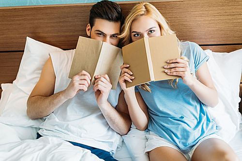 smiling couple looking out from books in bed