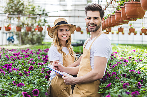 Young gardeners holding clipboards by flowers in greenhouse