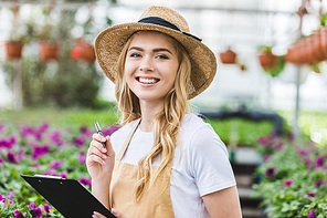 Blonde woman holding clipboard by flowers in greenhouse