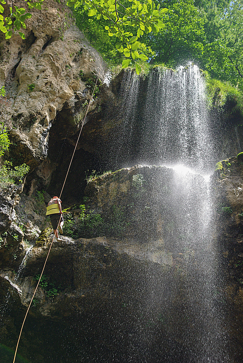 bottom view of man climbing up rope near waterfall, Russian Federation, Caucasus, July 2012