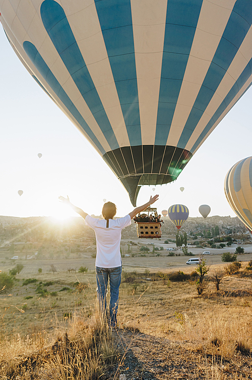 back view of man and hot air balloon flying in Goreme national park, fairy chimneys, Cappadocia, Turkey