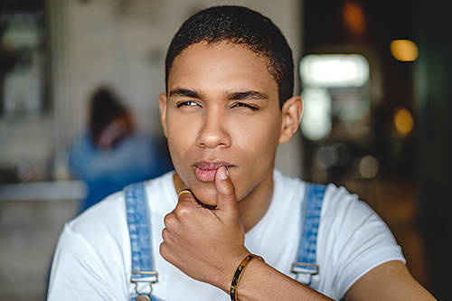 Thoughtful young man with hand by face sitting in cafe
