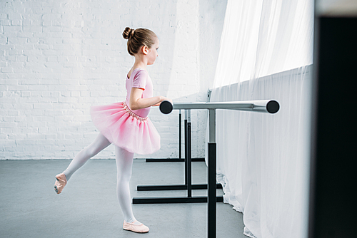 side view of child in pink tutu practicing ballet in studio