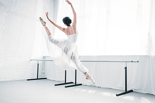 back view of graceful young ballerina in white dress dancing in ballet studio