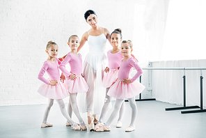 ballet teacher with cute little ballerinas smiling at camera in ballet school