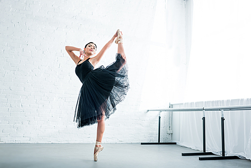 full length view of beautiful young ballerina practicing ballet in studio