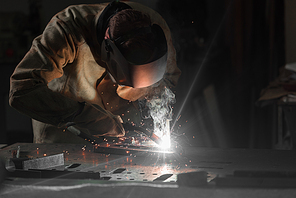 worker in protection mask welding metal at factory