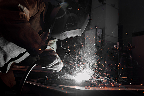 side view of worker in protection mask welding metal at factory