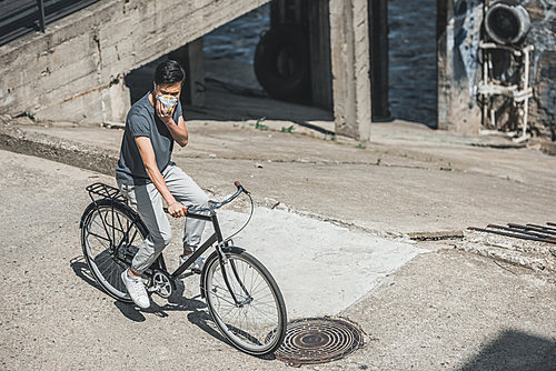 high angle view of asian teen in protective mask riding bicycle on bridge, air pollution concept