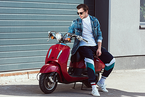 handsome young man in stylish vintage clothes sitting on scooter
