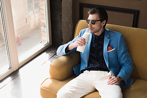 high angle view of handsome young man in stylish suit sitting on couch and drinking milk from bottle