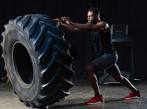 side view of muscular african american sportsman exercising with tyre