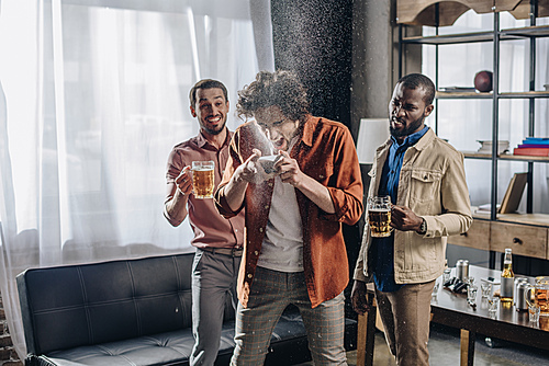 laughing multiethnic friends looking at man drinking beer from can
