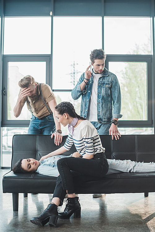 Men and woman worried about young fainted woman lying on sofa in office