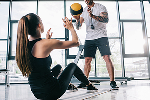 male personal trainer and sportswoman doing exercises with ball at gym