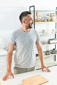 side view of adult man standing near table with cutting board on kitchen