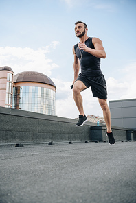 low angle view of handsome sportsman running and listening music with smartphone on roof