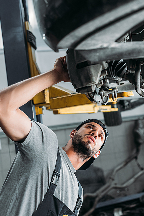 bottom view of workman in uniform repairing car in mechanic shop