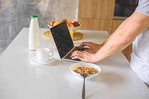 cropped image of young man using laptop at kitchen table with breakfast