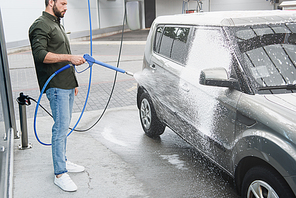 handsome man cleaning car at car wash with high pressure water jet