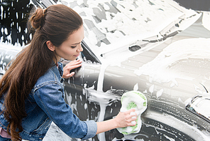 side view of attractive woman cleaning car at car wash with rag and foam