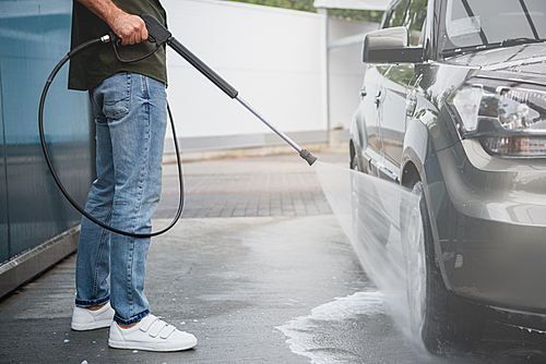 cropped image of man cleaning car at car wash with high pressure water jet