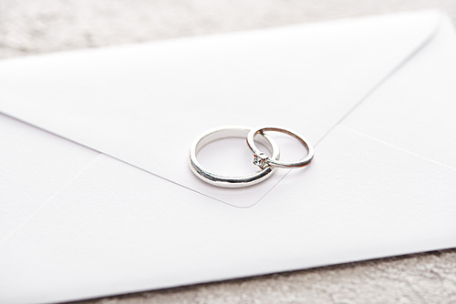 silver wedding rings on white envelope on grey textured surface