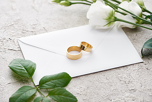 golden rings on white envelope near eustoma flowers on grey textured