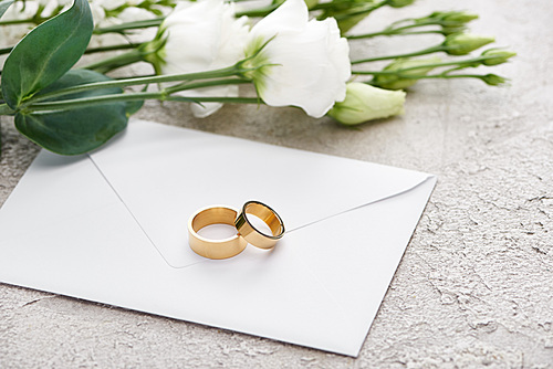 golden wedding rings on envelope near white eustoma flowers on textured surface