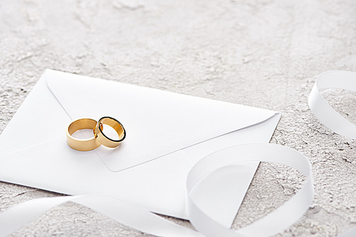 golden rings on envelope near white ribbon on grey textured surface