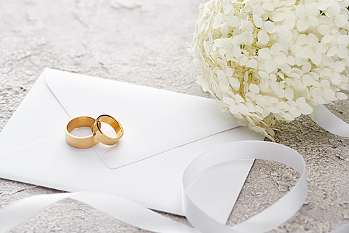 golden rings on envelope near white ribbon and Hortense flower on grey textured surface