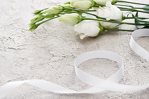 white eustoma flowers near ribbon on textured surface, wedding concept